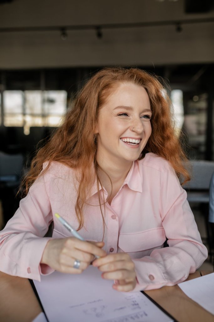 Joyful red-haired woman laughing while working in an office environment.