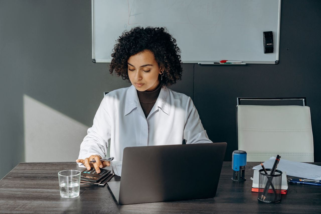 Focused woman in office setting working on laptop with documents, creating a professional atmosphere.