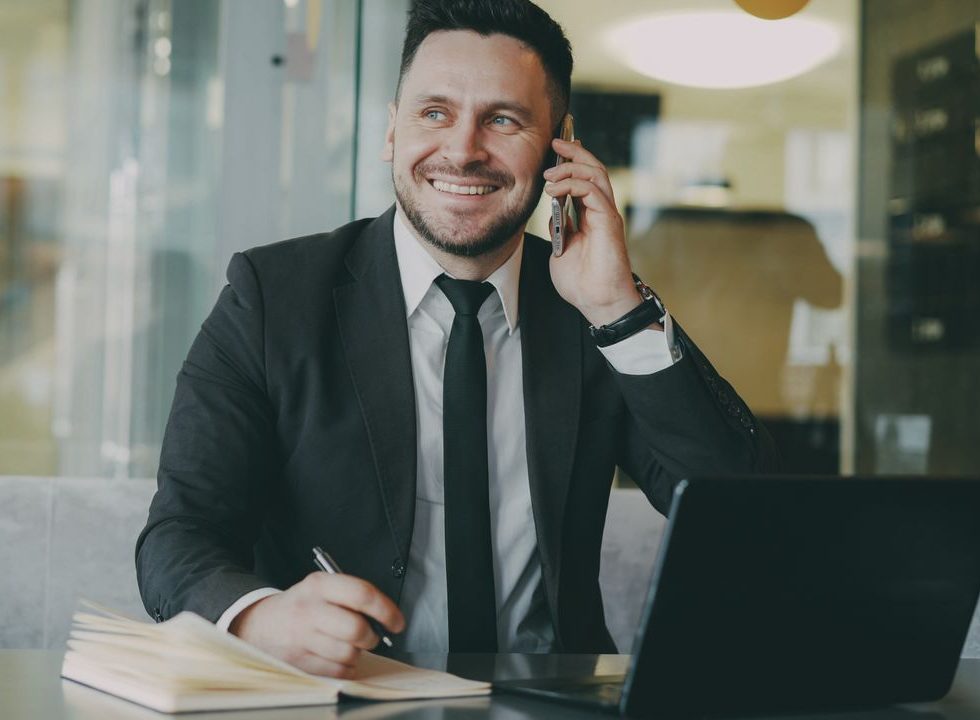 Smiling businessman making a phone call while working in a modern office environment.