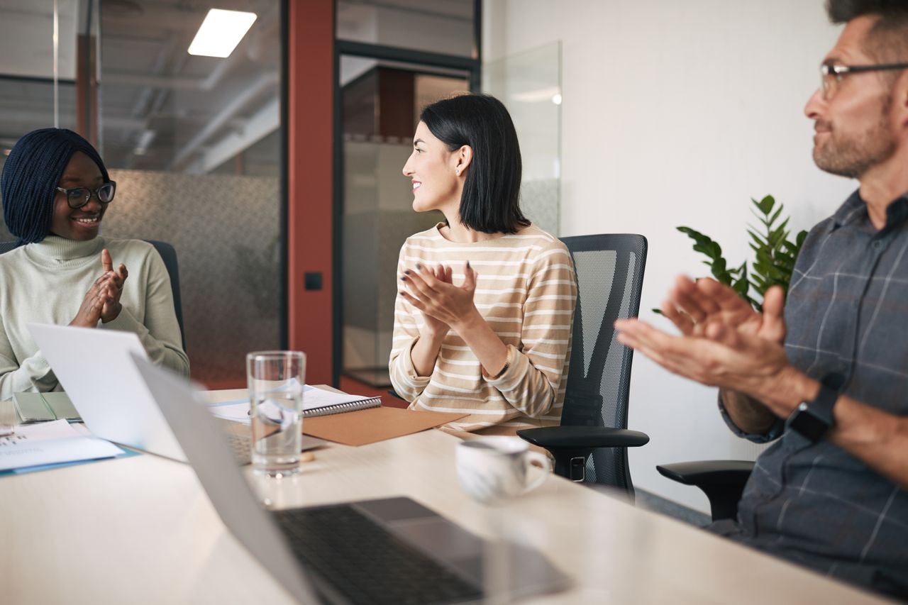 A diverse group of colleagues clapping during a meeting in a modern office.